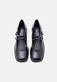 Μαύρα vegan παπούτσια Mary Jane από δερματίνη, με τετράγωνη μύτη, διπλή λουριά με αγκράφες και γυαλιστερό φινίρισμα. Ομαλή υφή σε όλη την επιφάνεια.