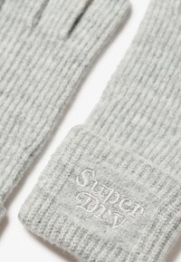Guantes de punto gris con textura acanalada, que presentan un pequeño logo bordado en blanco "Superdry" en el puño. Material suave y cálido.