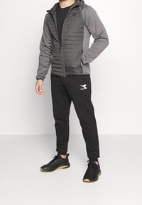 Herrjacka i mörkgrått med kviltad front, långa ärmar och huva. I kombination med svarta träningsbyxor och svarta sneakers med gummisulor.