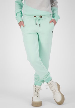Mintgrüne Sweatpants mit elastischem Bund, Kordelzug und Taschen. Getragen mit weißen Schnürstiefeln, die eine klobige beigefarbene Sohle haben.