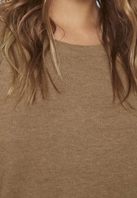 Pull en tricot marron avec un col côtelé, présentant une texture douce et fine ainsi qu'une coupe décontractée. Le tissu semble chaud et confortable.