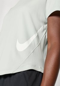 Svetlozelené športové tričko s okrúhlym výstrihom, krátkymi rukávmi a veľkým bielym logom Nike na boku. Má hladkú textúru.