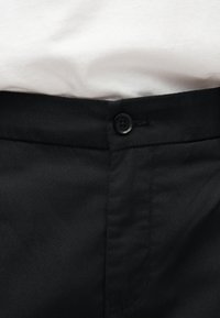 Περιοχή της μέσης μαύρου παντελονιού με κουμπί μαύρου χρώματος, συνδυασμένη με λευκό πουκάμισο που είναι μπαρταρισμένο μέσα.