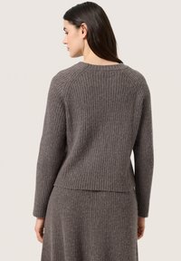 Ribbed, knit sweater in a muted gray tone with long sleeves and a round neckline, featuring a slightly cropped design and textured fabric.