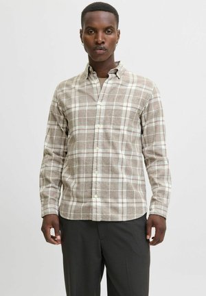 Camisa de cuadros marrón y crema con botones y mangas largas, bolsillo en el pecho y textura de tela suave. Combinada con pantalones de color oscuro.