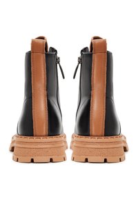 Bottes chevilles en cuir noir avec panneaux latéraux marron, semelles en caoutchouc texturées et fermetures éclair à l'arrière. Présentent un design épais pour une meilleure accroche.