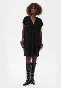 Czarna sukienka o krótkim rękawie z dekoltem w serek i luźnym krojem. Połączona z błyszczącymi, czarnymi kozakami za kolano oraz kolorowymi bransoletkami na nadgarstku.