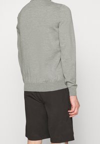 Pull gris clair en maille avec un col rond, des manches longues et une taille ajustée, associé à un short foncé, vu de dos.