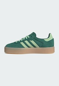 Zöld velúr sneaker világoszöld csíkokkal, párnázott nyakkal és textúrált gumitalpával. A fűzők megegyeznek a felsőrész színével.
