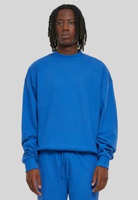 Felpa blu in cotone con scollo rotondo, maniche lunghe e vestibilità rilassata. Tessuto a trama con polsini a coste. Indossata con pantaloni abbinati.