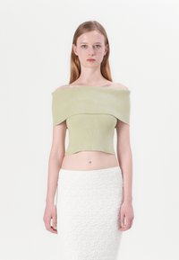 Top corto de canalé sin hombros en verde claro, con un diseño ajustado. Combinado con una falda blanca texturizada. Textura de tela suave.
