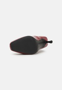 Červená lakovaná vysoká podpatková bota s špičatou špičkou, texturovanou černou podešví a štíhlým podpatkem. Design zdůrazňuje elegantní profil.