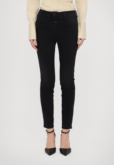 Jeans skinny noirs avec une texture lisse, taille haute et fermeture à bouton. Associés à des escarpins noirs à bout pointu et à des ourlets retroussés.