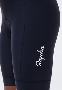 Cuissard de cyclisme noir avec le logo blanc "Rapha" sur la cuisse gauche, vue en gros plan du tissu et des coutures.