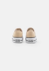 Baskets basses en toile beige avec semelles en caoutchouc blanc, rayures noires, et le logo "Converse All Star" sur le talon.