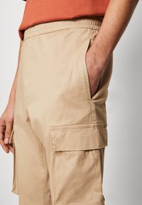Shorts cargo beige hechos de una tela ligera, con una cintura elástica, bolsillos laterales y un bolsillo cuadrado en la pierna.