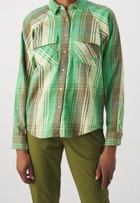 Zelená kostkovaná košile na knoflíky s dvěma kapsami na prsou, kombinace světle a tmavě zelených, hnědých a krémových pruhů. Měkká, texturovaná tkanina.