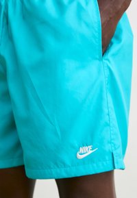 Bañador de Nike en color turquesa, hecho de material ligero, con cintura elástica y un acento del logo blanco en la parte inferior izquierda. Textura suave.