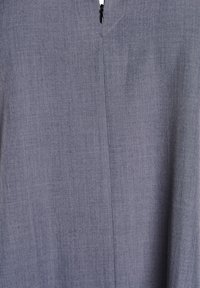 Šedá tkanina s jemnou strukturou a detailem šití. Obsahuje zipový uzávěr na výstřihu a zjednodušený tvar.