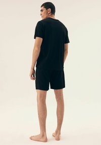 Czarny zestaw koszulki i szortów, wykonany z miękkiego materiału. Prosty design z krótkimi rękawami i okrągłym dekoltem. Brak widocznych wzorów lub akcentów.