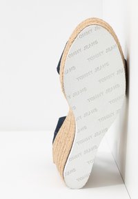 Semelle en caoutchouc blanche avec motif texte "Tommy Jeans" sur une sandale espadrille compensée avec une semelle intermédiaire en jute tressée et une tige bleu marine.