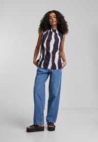 Débardeur sans manches bleu marine et blanc à rayures, avec des accents orange, associé à un jean large bleu clair et des sandales à plateformes noires.