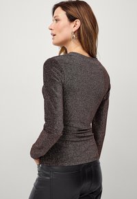 Top lungo a maniche, di un metallo scuro con un design aderente, caratterizzato da un collo rotondo e una finitura testurizzata, abbinato a pantaloni di pelle nera.