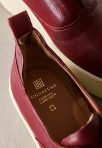 Bordowe skórzane mokasyny o teksturowanym wykończeniu, z kremową gumową podeszwą i wytłoczonym wewnętrznym logo "Signature Forever Comfort".