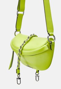 Lille limegrøn læder crossbody taske med sølvkæde-detail, tykk justerbar rem og metalspænder, vist mod hvid baggrund.