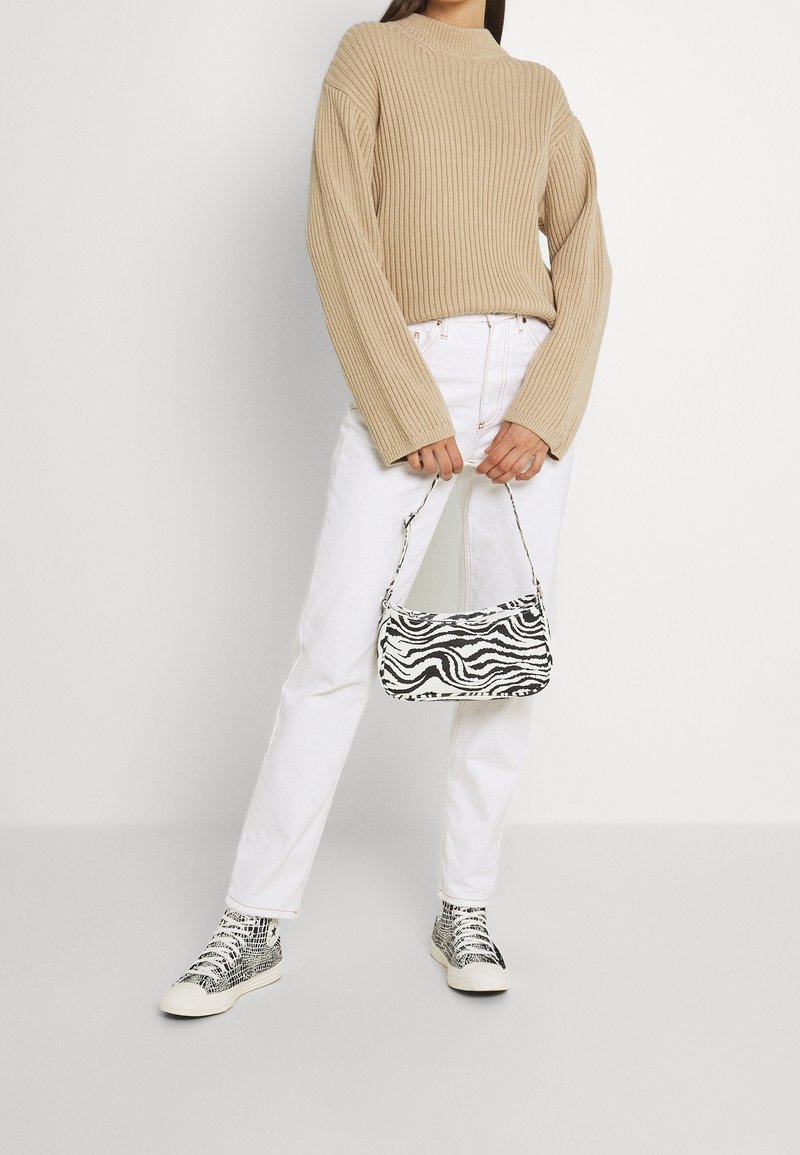 Beżowy sweter w prążki, białe jeansy z prostymi nogawkami, czarno-biała torebka w zebrę oraz wzorzyste trampki za kostkę.