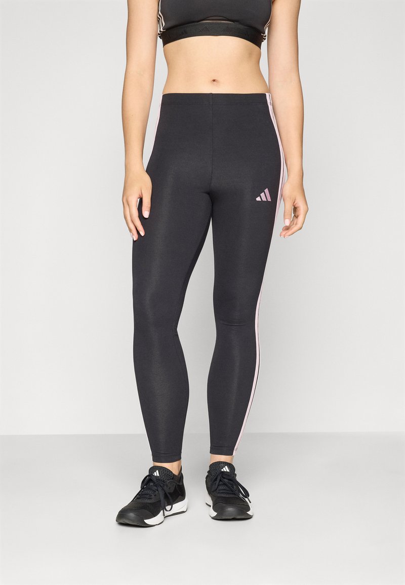 Leggings atléticos pretos com riscas laterais rosas, apresentando um design ajustado e um pequeno logotipo da Adidas na coxa esquerda, feitos de um material elástico.