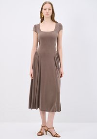 Braunes Jersey-Kleid mit Stretch, quadratischem Ausschnitt, kurzen Puffärmeln, gerafftem Taillenbereich und knöchellangem Saum; kombiniert mit braunen Riemchensandalen.