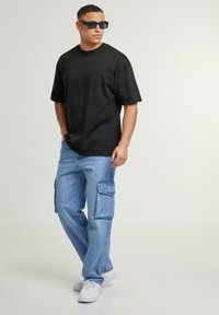 Black cotton t-shirt, relaxed fit, paired with light blue denim cargo pants featuring large side pockets, and white sneakers.
