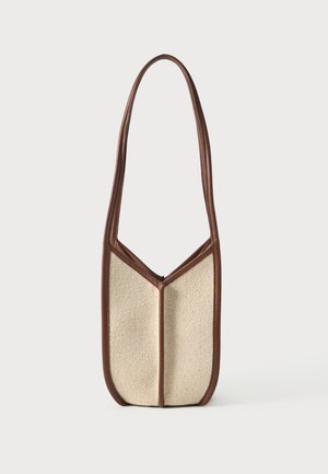 Beige textured shoulder bag with dark brown leather trim and long strap, standing upright on a plain light background.