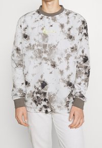Sudadera tipo crewneck en un patrón de teñido anudado en gris y blanco; cuenta con mangas largas, puños acanalados y un pequeño logotipo amarillo en el frente.
