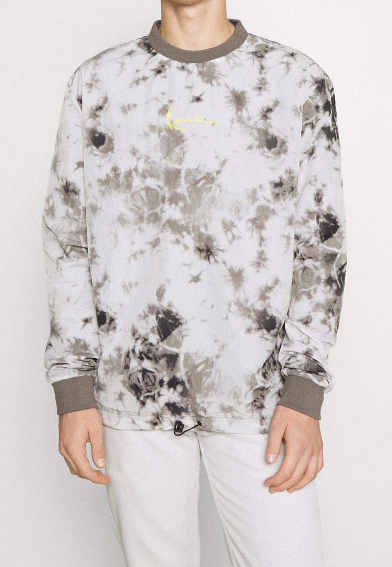 Sudadera tipo crewneck en un patrón de teñido anudado en gris y blanco; cuenta con mangas largas, puños acanalados y un pequeño logotipo amarillo en el frente.