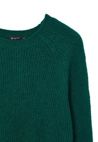 Grüner gestrickter Pullover mit rundem Ausschnitt, gerippter Textur und Raglanärmeln. Etikett sichtbar mit Markenname und Größe XS/S.