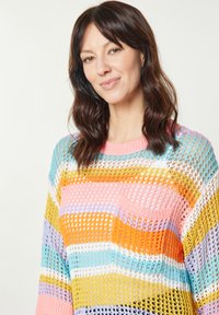 Sweter dzianinowy o luźnym, siatkowym wzorze z wielokolorowymi pionowymi paskami w odcieniach pomarańczowym, różowym, niebieskim, purpurowym i żółtym. Z przodu kieszeń.