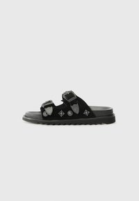 Black suede slide sandal with two adjustable straps, featuring decorative hardware and a textured rubber sole with a ridged edge.