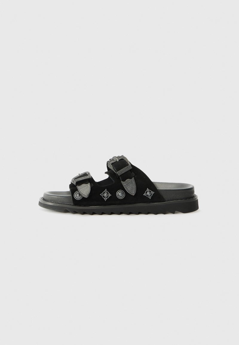 Black suede slide sandal with two adjustable straps, featuring decorative hardware and a textured rubber sole with a ridged edge.