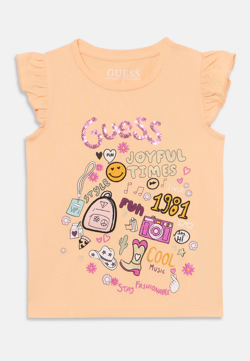 Camiseta de algodón orgánico color melocotón con mangas con volantes. Presenta diseños impresos coloridos, incluyendo una mochila, una cámara y elementos de texto.