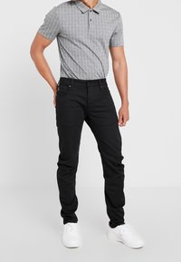 Grå randig piké med krage, kombinerad med svarta jeans. Vita sneakers fulländar outfiten och framhäver de eleganta linjerna och den åtsittande stilen.