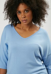 Maglione azzurro chiaro lavorato a maglia con scollo a V, maniche a tre quarti e una texture morbida, caratterizzato da una vestibilità rilassata per il massimo comfort.