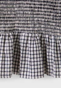 Tissu à carreaux noir et blanc avec smocks élastiqués froncés en haut et ourlet à volants en bas.