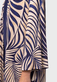 Lättviktskimono i tyg med beige och marinblå palmbladsmönster, med vida ärmar och en mjuk textur.