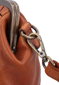 Smeđa kožna torba izbliza, s metalnom kopčom, teksturiranom površinom i metalnim akcentima. Mekan, zakrivljen oblik na otvore.
