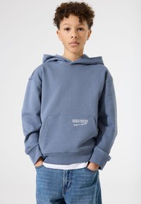 Blaues Hoodie mit einer vorderen Tasche, mit weißem Text "Inspiring Landscapes Trekking Team 1972." Strukturiertes Material, verstellbare Kapuze.