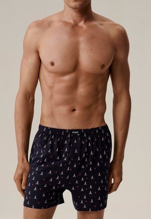 Granatowe bokserki z białym wzorem drzewa i czerwonych wiśni, wykonane z miękkiego materiału, z elastycznym pasem i zapięciem na guziki z przodu.