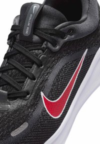Κοντινό πλάνο μαύρου παπουτσιού τρεξίματος Nike Stellar Ride με μαύρα κορδόνια, κόκκινο λογότυπο Swoosh και λευκή σόλα.