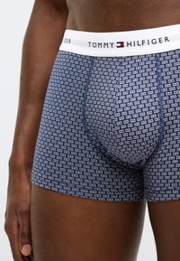 Mørkeblå boxershorts med et gentagende hvidt geometrisk mønster og en elastisk linning med "TOMMY HILFIGER" logo. Blød tekstur.